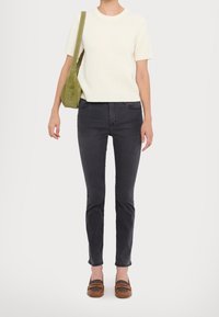 Maglione corto a coste di colore crema, jeans slim-fit grigi scuri, mocassini marroni con dettagli a fantasia e una borsa a spalla in suede verde.