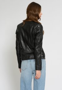 Schwarze Lederjacke mit taillierter Passform, gesteppten Schultern und glatter Textur, kombiniert mit hellblauen hochgeschnittenen Jeans.
