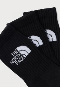 Μαύρες ριγωτές κάλτσες με αντίθετο λευκό λογότυπο και γραφικά βουνού στην εξωτερική πλευρά, κατασκευασμένες από μαλακό πλεκτό ύφασμα.