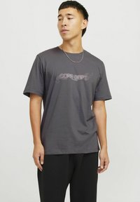 Grijze katoenen t-shirt met korte mouwen, voorzien van een grafische print in lichtroze met de tekst "CORE DEPT" over de borst. Rechte, ronde halslijn.