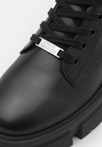 Botín de cuero negro hasta el tobillo con superficie texturizada, cordones negros y una etiqueta metálica plateada con la inscripción "STEVE MADDEN". Suela negra gruesa.