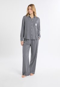 Dwuczęściowa piżama w paski w kolorze granatowym i białym, zawierająca zapinaną na guziki bluzkę z kieszenią oraz dopasowane szerokie spodnie, wykonane z miękkiego materiału.