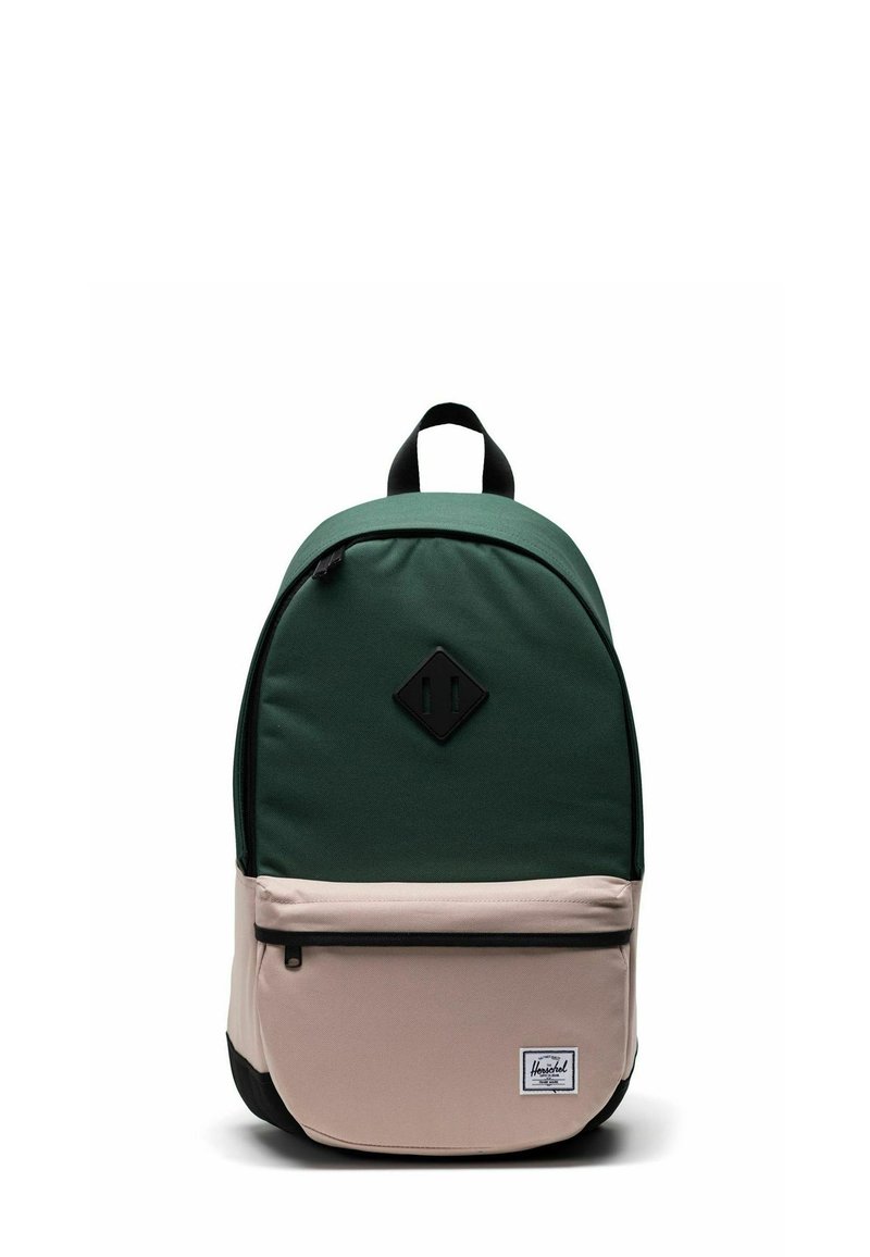 Sac à dos vert et beige de forme arrondie, fabriqué en tissu, avec une poche avant, une fermeture éclair noire et un écusson logo sur le bas de l'avant.