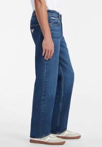 Jeans de mezclilla oscuros de pierna recta con cintura alta y un sutil desgastado. Cuenta con un bolsillo trasero con logo y costuras en contraste.
