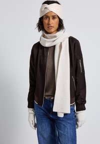 Brun bomberjacka med en krämfärgad scarf, stickad huvudband, ljusbrun tröja och gråa handskar, i kombination med blå jeans.