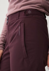 Bordeaux farvede bukser med en glat tekstur, der har en sidetask og diskret logo detaljer. Knappen til lukning i taljen, designet til udendørs brug.