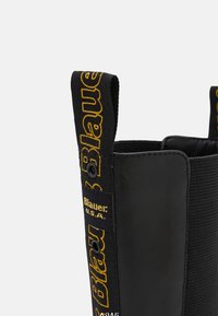 Botte en cuir noir avec panneau latéral élastique, languette de tirage marquée du texte "Blauer U.S.A." en broderie jaune sur tissu noir.