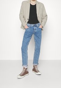 Beige károvaný blejzr, černé tričko, světle modré denimové džíny, vyhrnuté manžety, hnědé vysoké tenisky s bílými akcenty a tkaničkami.