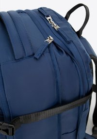 Námořnická modrá batoh s polstrovanou tkaninou, dvojitým zipem, nastavitelnými popruhy a černým popruhem pro zvýšení podpory.