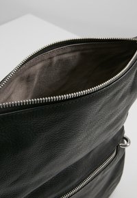 Černá kožená kabelka s texturovaným povrchem, se stříbrným zipem, podšívkou uvnitř a vnější kapsou na zip.