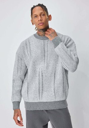 Pull gris tricoté avec des rayures verticales, col rond et poignets côtelés. Comprend un ourlet gris uni et une finition texturée.