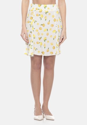 Gonna bianca a linea A con stampa gialla di limoni e foglie, indossata con tacchi slingback bianchi con punta appuntita su una modella in piedi.