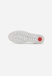White sneaker sole with textured pattern, featuring a circular red accent near the heel, smooth white material, and indented grip design.