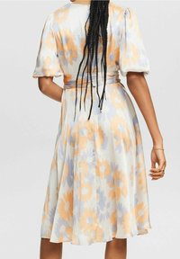 Robe florale avec des manches bouffantes courtes, une taille cintrée et une jupe évasée. Le tissu est léger avec des motifs de fleurs orange et bleues sur un fond blanc.