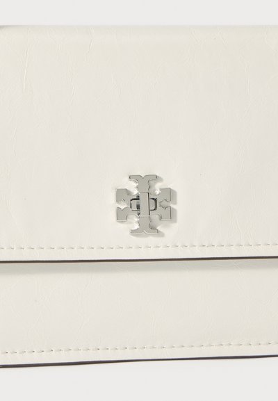 Biały portfel z sztucznej skóry o teksturowanej powierzchni, z metalowym zapięciem w srebrnym kolorze z motywem krzyża oraz widocznym przeszyciem wzdłuż krawędzi.