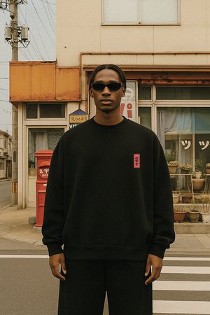 Young man wearing black sweatshirt and sunglasses standing on a crosswalk in front of a vintage building with potted plants and a red mailbox.
