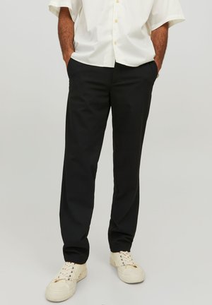 Pantaloni neri a gamba dritta realizzati in misto cotone, con passanti per cintura, tasche laterali e una finitura pulita. Indossati con sneakers bianche.