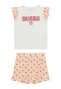 Bijela košulja kratkih rukava s crvenim grafičkim natpisom "GUESS love" i naboranim breskvastim rukavima. Breskvaste kratke hlače s crvenim uzorkom trešanja i naboranim rubom.