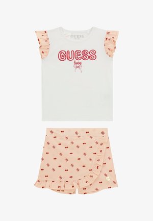 Witte korte mouwen shirt met een rode "GUESS love" graphic en zalmroze rimpels aan de mouwen. Perzikkleurige shorts met een rood kersenpatroon en een gerimpelde zoom.