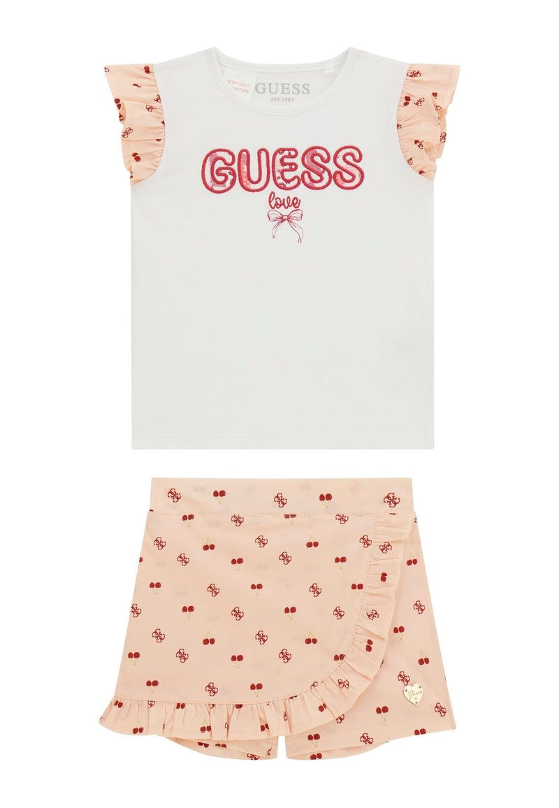 Bijela košulja kratkih rukava s crvenim grafičkim natpisom "GUESS love" i naboranim breskvastim rukavima. Breskvaste kratke hlače s crvenim uzorkom trešanja i naboranim rubom.