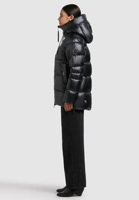 Chaqueta acolchada negra con un acabado brillante y acolchado, capucha y bolsillos con cremallera, combinada con jeans rectos negros y elegantes botines.