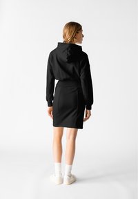 Svart hoodie med en åtsittande design och känguruficka, i kombination med en knälång svart kjol. Vita sneakers och ribbade strumpor fulländar looken.