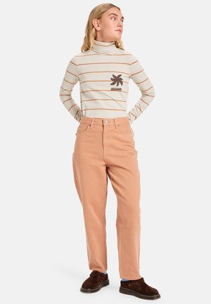 Gestreepte, beige coltrui met een bruine logo; gecombineerd met perzikkleurige, losse broek. Bruine instapschoenen maken de outfit af.
