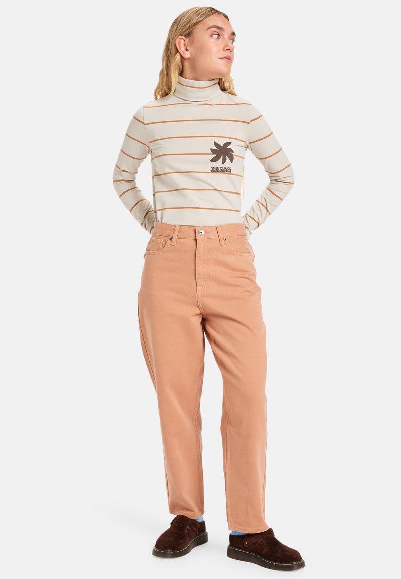 Suéter de cuello alto a rayas en color beige con logo marrón; combinado con pantalones sueltos en color durazno. Unos zapatos marrones tipo mocasín completan el conjunto.
