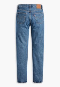 Jean en denim bleu classique vu de dos avec deux poches cousues et un patch de marque en cuir marron sur la ceinture.