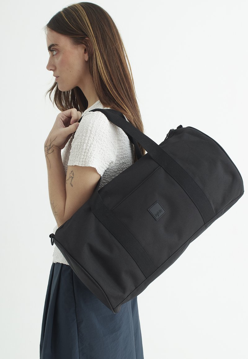 Svart duffelväska i slitstarkt tyg. Rundad form, platta sidor och två långa remmar. Har en liten logotyp framtill.