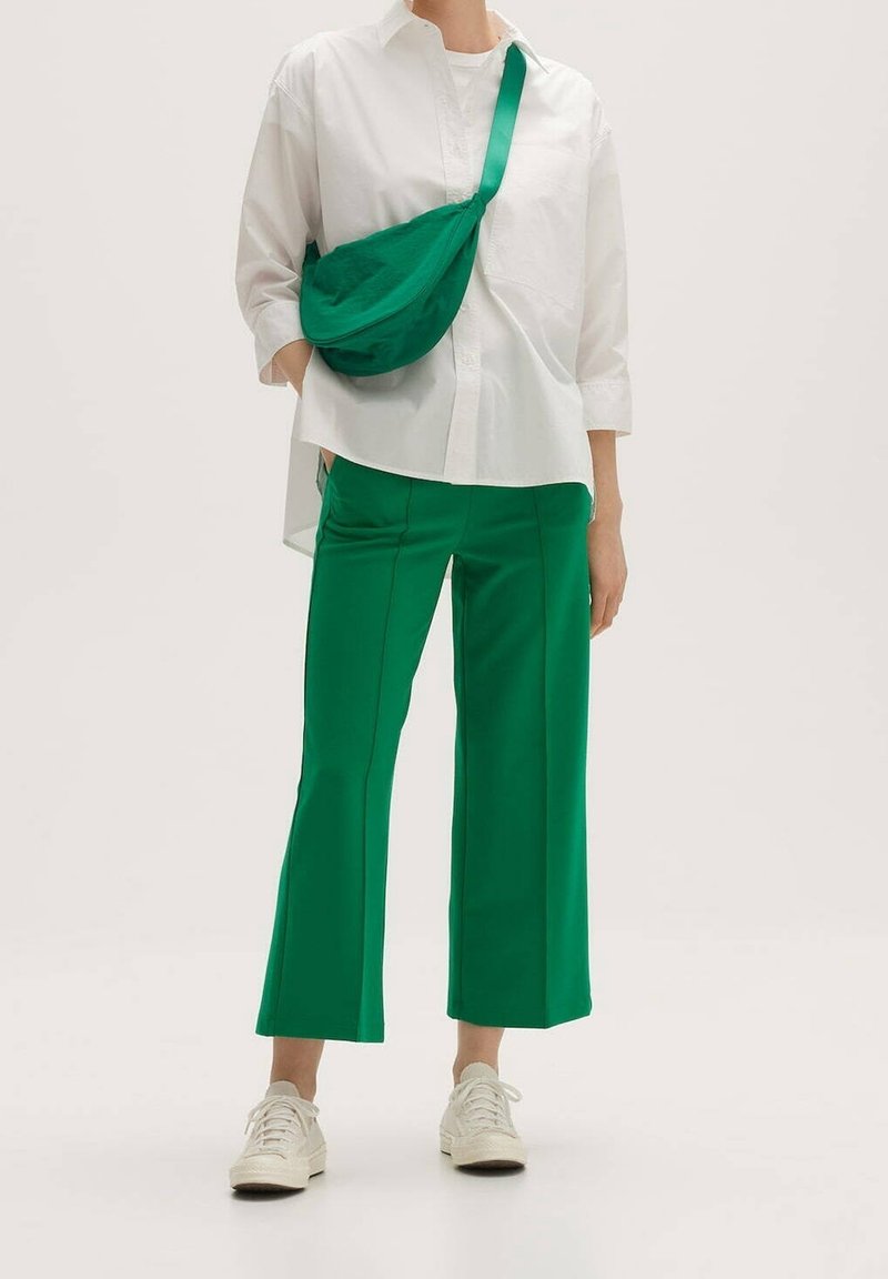 Bílé oversized košilové triko, zelené široké kalhoty a zelená crossbody taška, doplněné o bílé tenisky. Hladké textury a jednoduchý design.