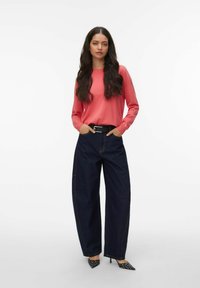 Haut corail à manches longues associé à un pantalon en denim foncé à jambes larges. Ceinture noire et talons à pois complètent le look. Tissu lisse et coupe décontractée.