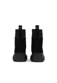 Botines de ante negros con cuellos de punto acanalado, suelas de goma negras gruesas y tiradores de logo en contraste en la parte trasera.
