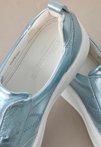 Metalické světle modré slip-on boty s bílou podrážkou, mají hladký povrch, minimální šití a vycpaný vnitřek pro pohodlí.