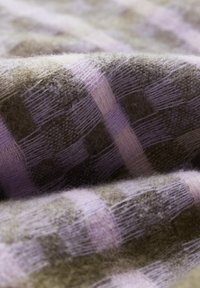 Tissu en laine présentant un motif tartan avec différentes textures. Les couleurs incluent un vert doux et un lavande clair, mettant en valeur la douceur et la profondeur.