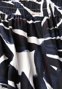 Tissu imprimé avec de vifs motifs abstraits noirs, bleu marine et blancs, doté d'une taille élastique et d'une finition douce et texturée.