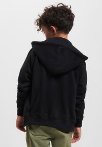 Sweat à capuche noir en matière douce et de poids intermédiaire. Il dispose d'une poche kangourou et de poignets côtelés. La vue arrière montre une coupe décontractée et un ourlet.