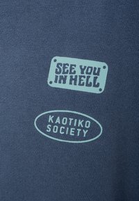 Camiseta de algodón azul que presenta dos textos: "TE VEO EN EL INFIERNO" en un diseño rectangular y "SOCIETY KAOTIKO" en un óvalo, ambos en fuente de color azul claro.
