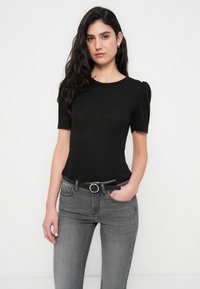 Μαύρο πλεκτό κοντομάνικο τοπ με στρογγυλή λαιμόκοψη και υφασμάτινη υφή, συνδυασμένο με γκρι τζιν και μαύρη ζώνη με στρογγυλή αγκράφα.