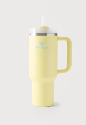 Grand gobelet de voyage isolant Stanley jaune avec poignée, couvercle transparent et paille blanche sur un fond clair uni.