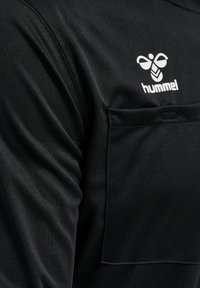 Sort atletisk t-shirt med en glat, strækbar tekstur. Har en frontlomme og et hvidt Hummel-logo på brystet.