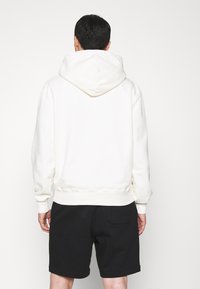 Felpa in pile crema con cappuccio grande e polsini a costine, abbinata a pantaloni corti neri. Morbido al tatto, vestibilità rilassata e design minimalista.
