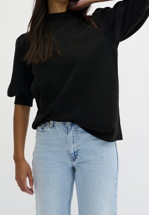 Haut noir à manches courtes avec un col montant, tissu texturé et coupe décontractée, associé à un jean taille haute bleu clair.