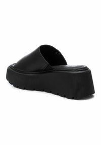 Zapatilla de plataforma negra con un upper liso y una suela de goma gruesa y estriada. El diseño presenta un talón cerrado y una plantilla contorneada.