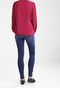 Fuchsiablus med lång ärm och strukturerat mönster, kombinerad med mörkblå tajta jeans. Svarta ballerinas fulländar outfiten.