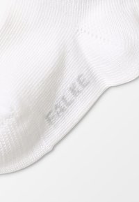 Calcetín blanco hasta el tobillo, hecho de un material suave y elástico. Presenta una textura acanalada y un logo impreso en gris claro cerca del dedo del pie.