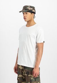 Tricou alb cu mânecă scurtă și guler rotund, asortat cu pantaloni scurți cargo camuflaj. O șapcă camuflaj se află pe cap, având o noi plată și o bandă.