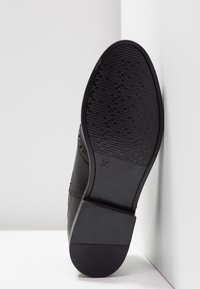 Semelle de chaussure noire avec un motif de grip texturé et une forme arrondie. Présente une finition lisse et un marquage de taille "37" sur le côté.