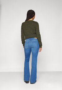 Maglione corto verde oliva con righe orizzontali testurizzate, abbinato a jeans a zampa d'elefante blu con tasche posteriori e vita aderente.