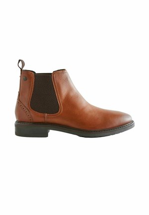 Bota Chelsea de cuero marrón con paneles laterales elásticos, superficie texturizada y un tirador. Tacón bajo con una suela de goma negra.